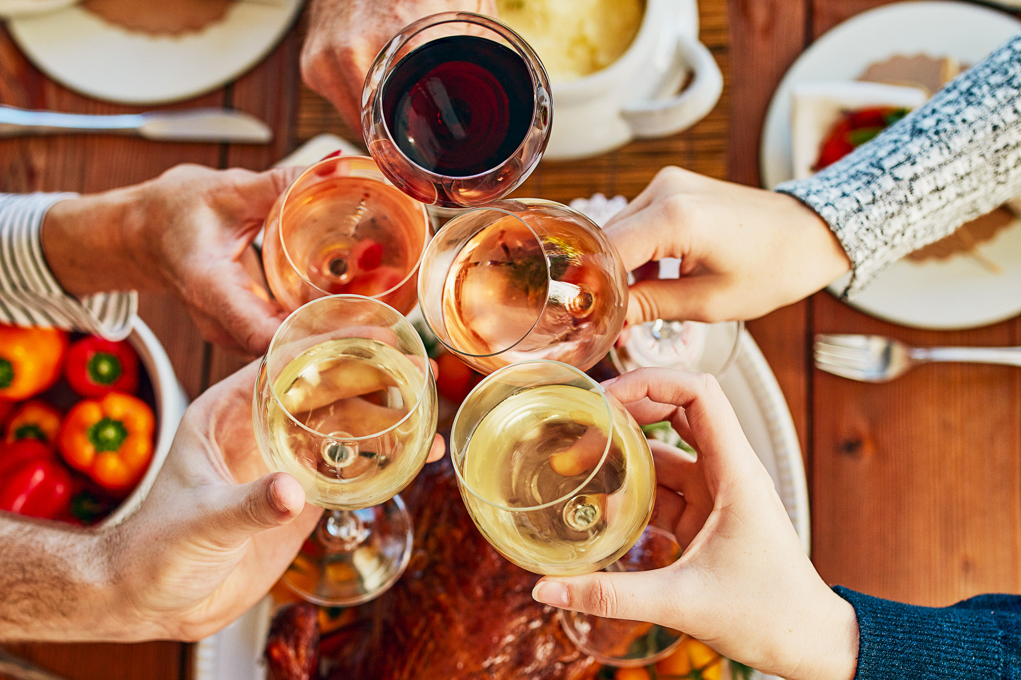 hands of five people toasting with wine glasses over a table with Thanksgiving food.